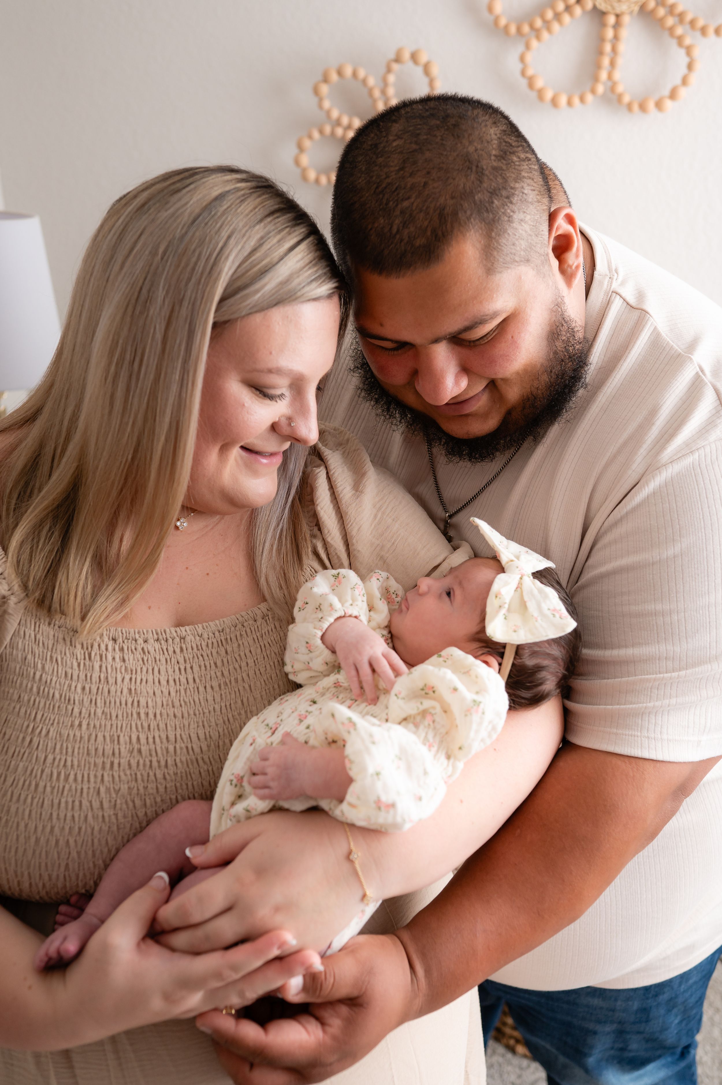 New parents lovingly gaze at their newborn baby girl dressed in white lace outfit with bow headband.
