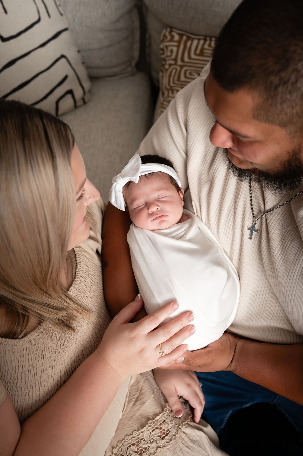 New parents lovingly gaze at their swaddled newborn baby girl wearing a white bow headband.