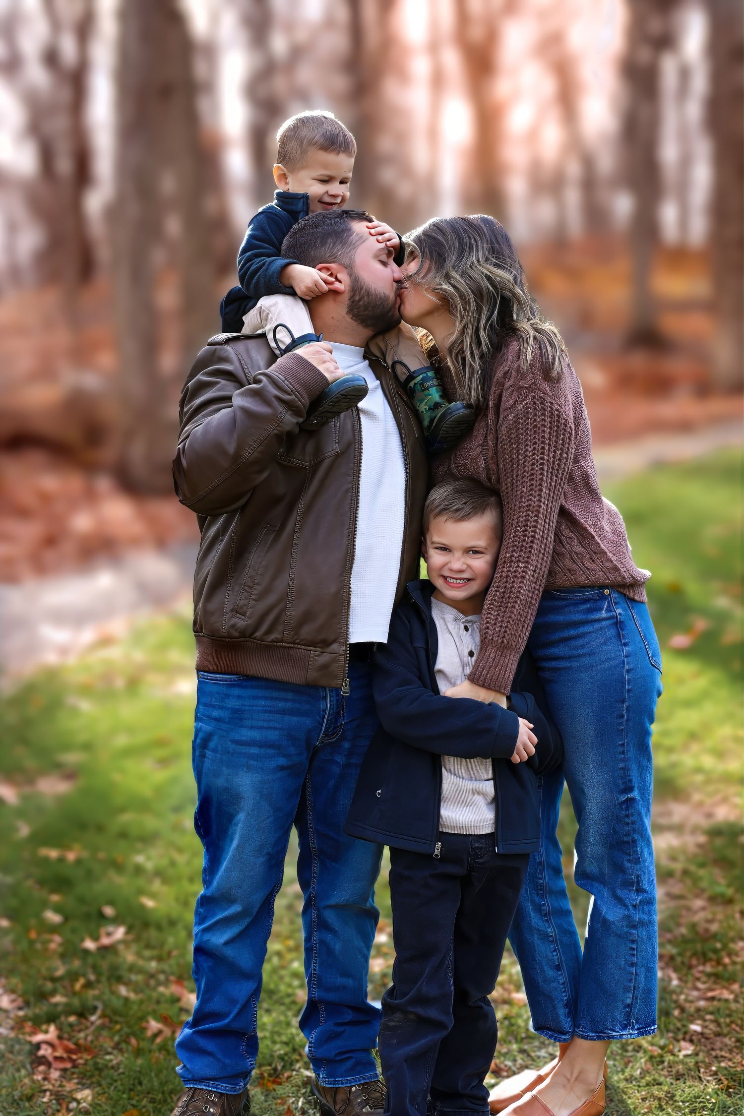 A loving family shares an intimate moment together outdoors during autumn with fallen leaves on the ground.