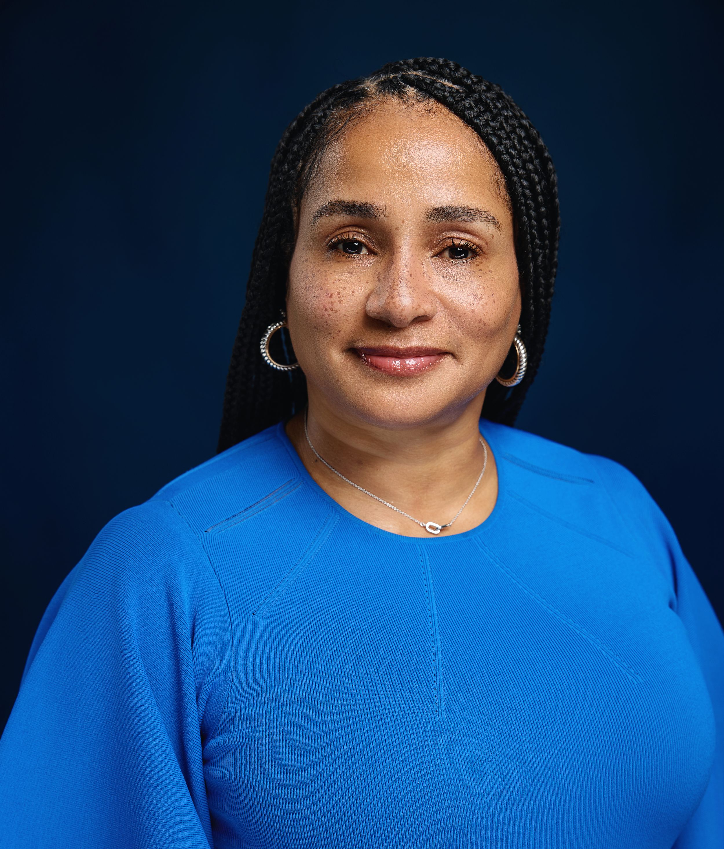 Portrait series against dark blue background showing warm smile and braided hairstyle.