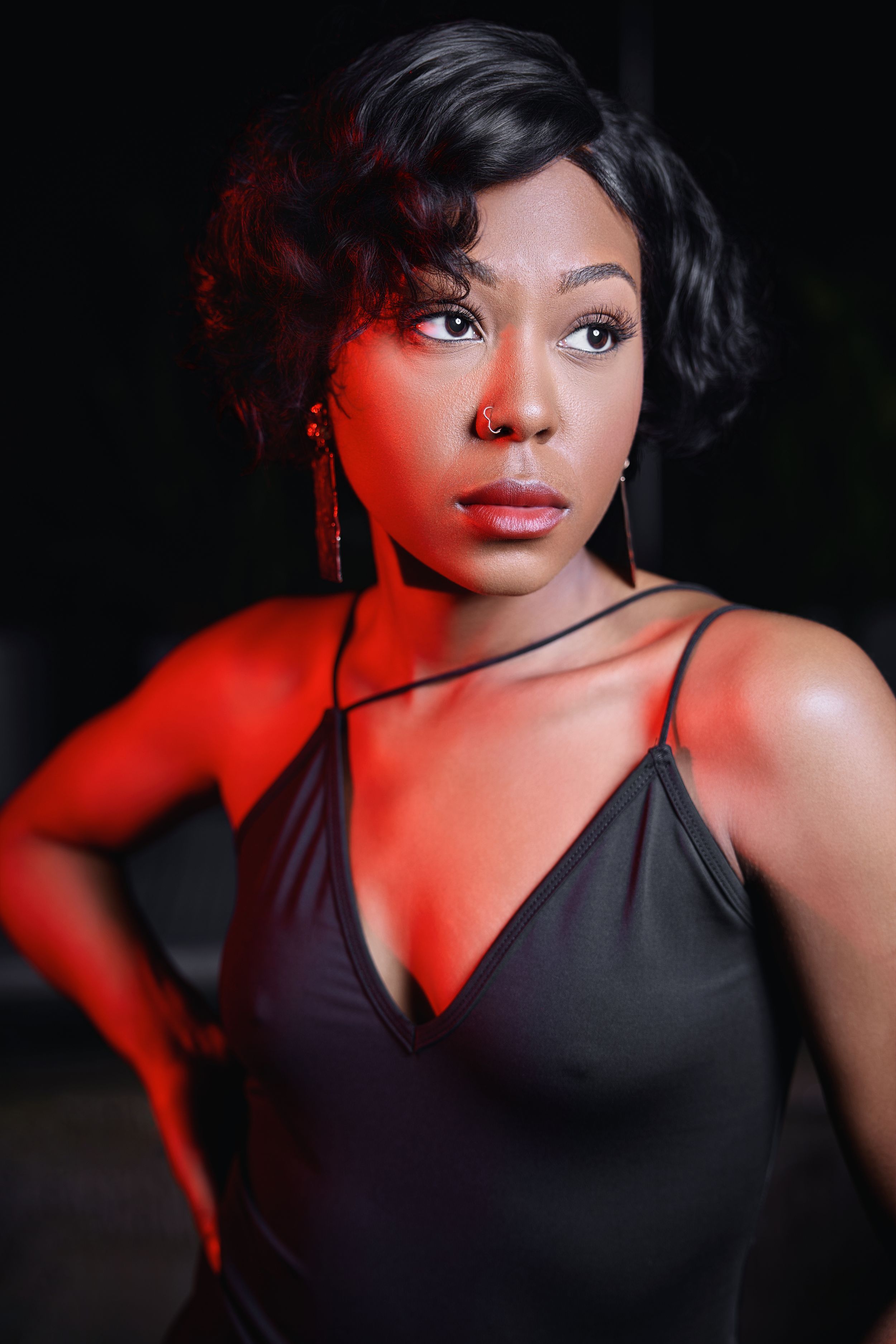 Dramatic portrait with red lighting and black dress against dark background.