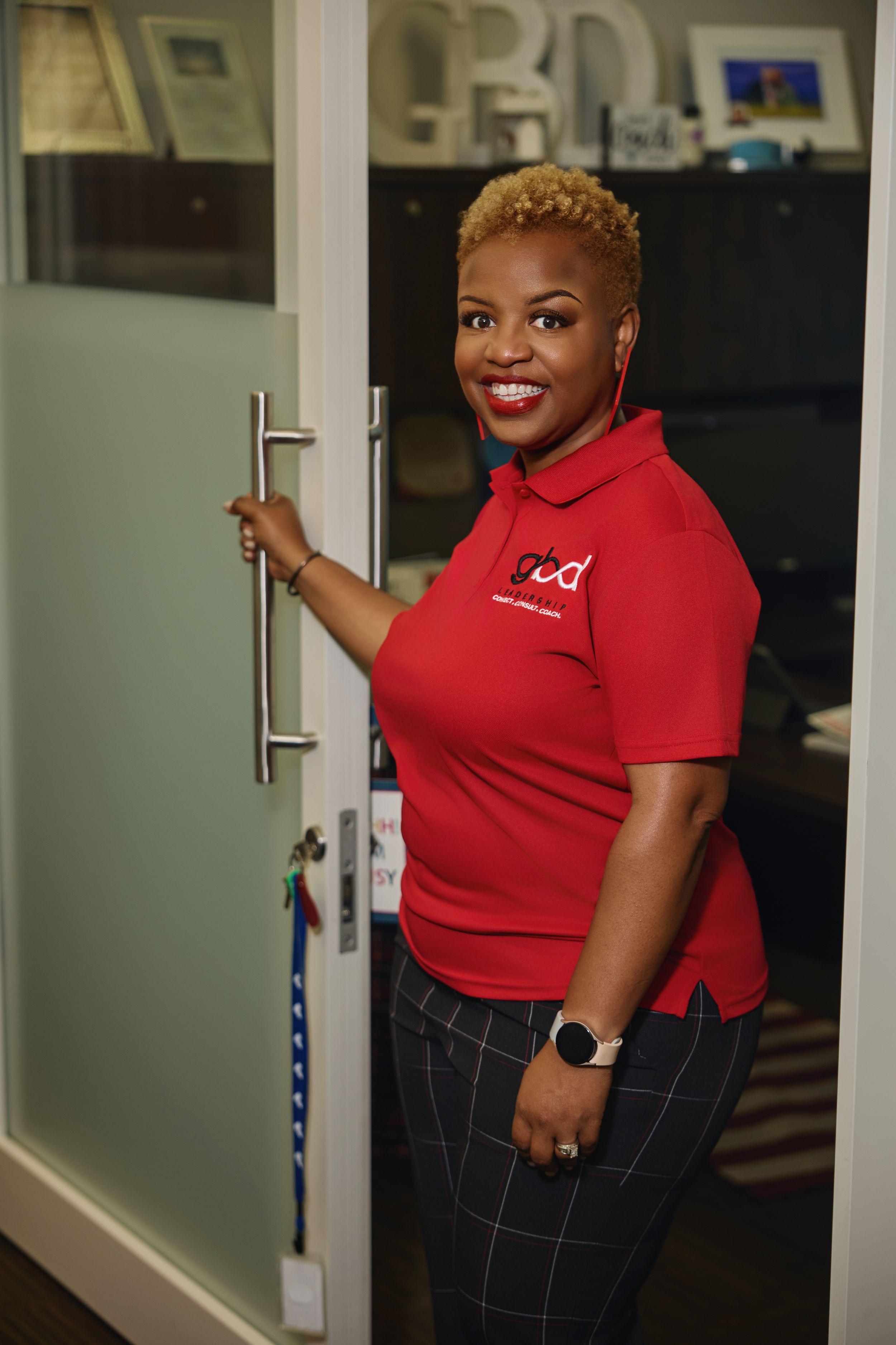 Professional in red polo shirt and plaid pants posing in office setting.