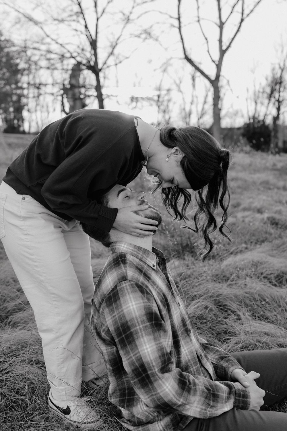 Black and white photo of a romantic outdoor moment between two people in a field with bare trees in the background in Frederick Maryland