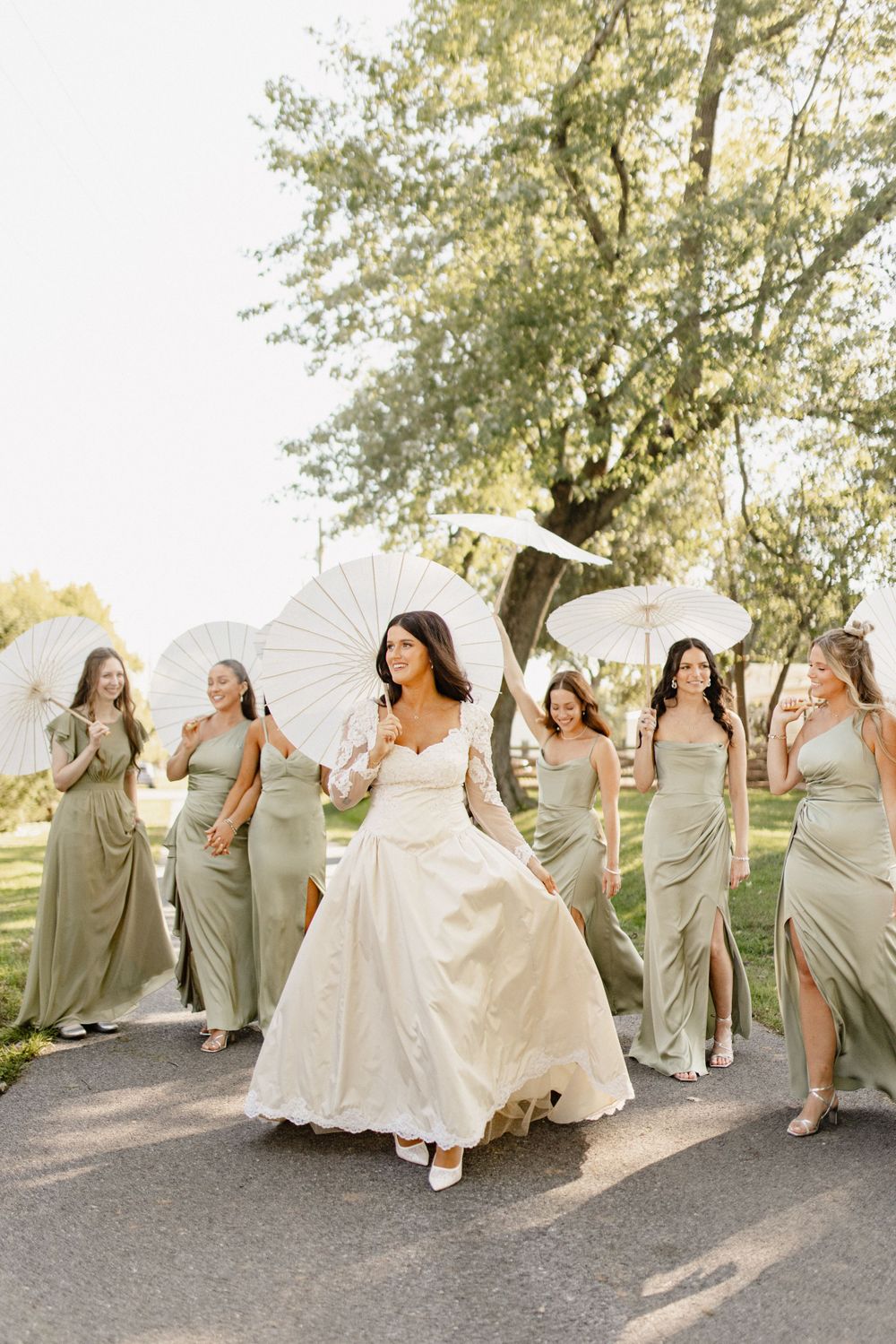 Wedding party laughs and dances together in a romantic outdoor setting with bridesmaids in sage dresses.