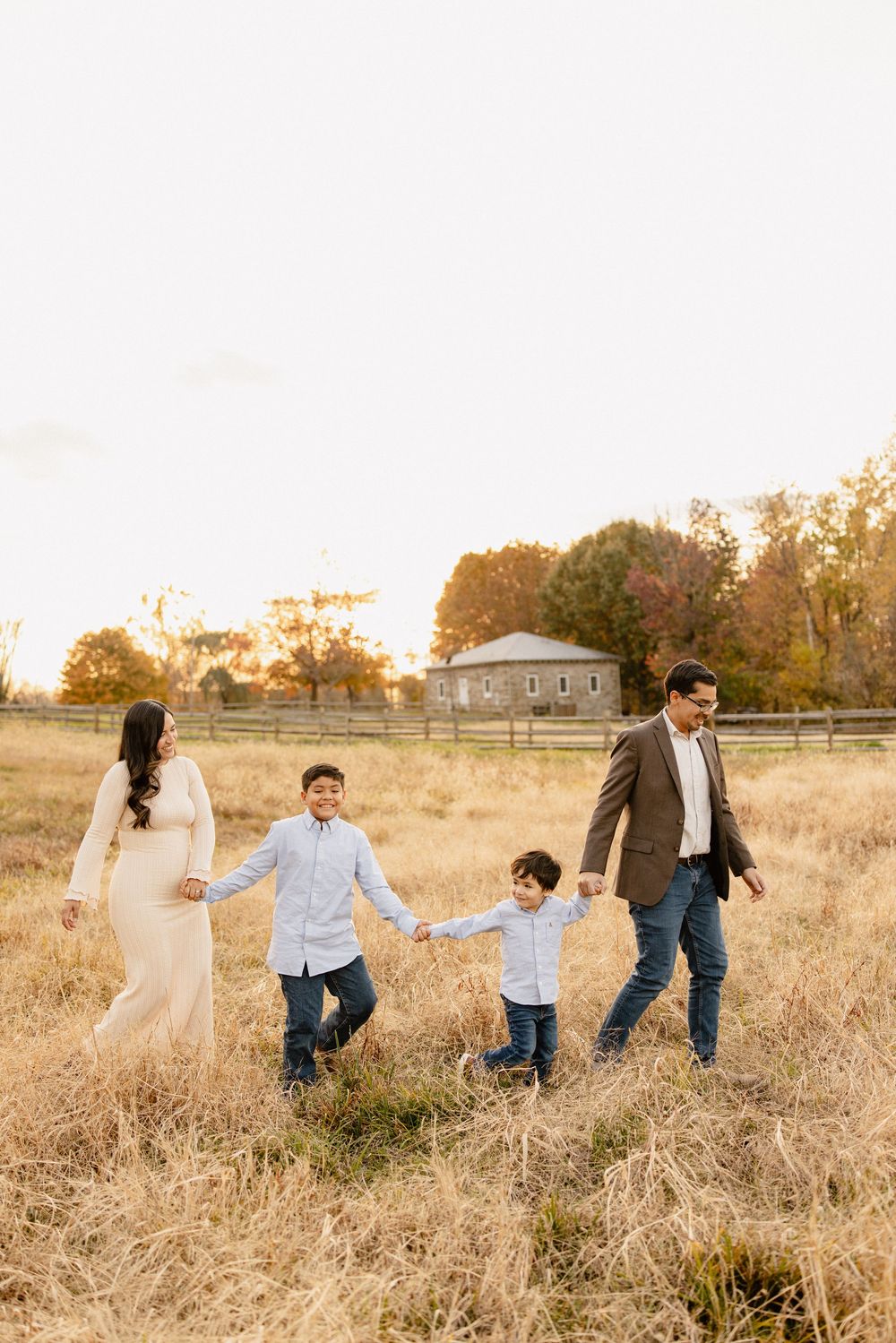 A family walks together through a golden autumn field at sunset, creating a joyful outdoor scene in Frederick Maryland.