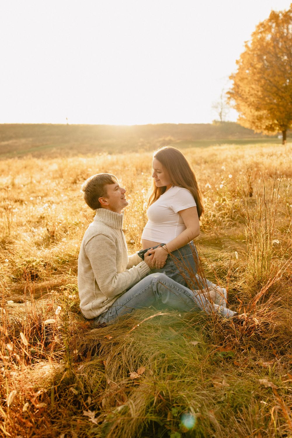 Two people sit together in a golden sunlit meadow during sunset, creating a warm and intimate outdoor portrait in Frederick Maryland.