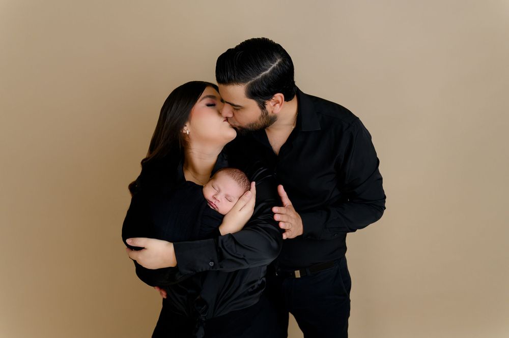 Intimate maternity photo session with couple in black outfits against neutral backdrop.