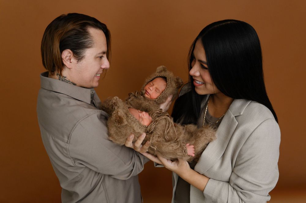 Cozy family photoshoot with matching gray outfits against warm brown background.