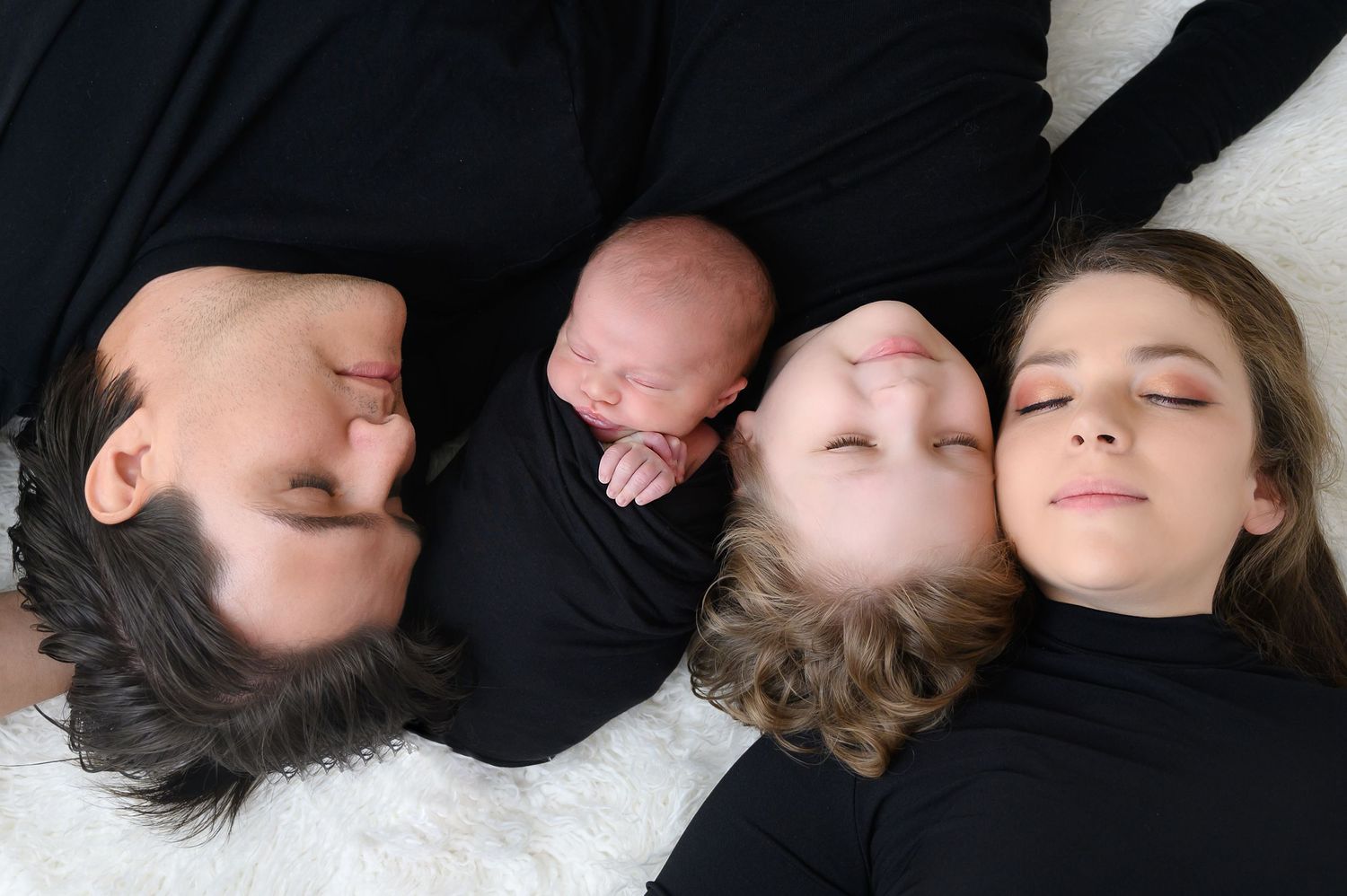 Family members laying down close together on black background in artistic portrait.