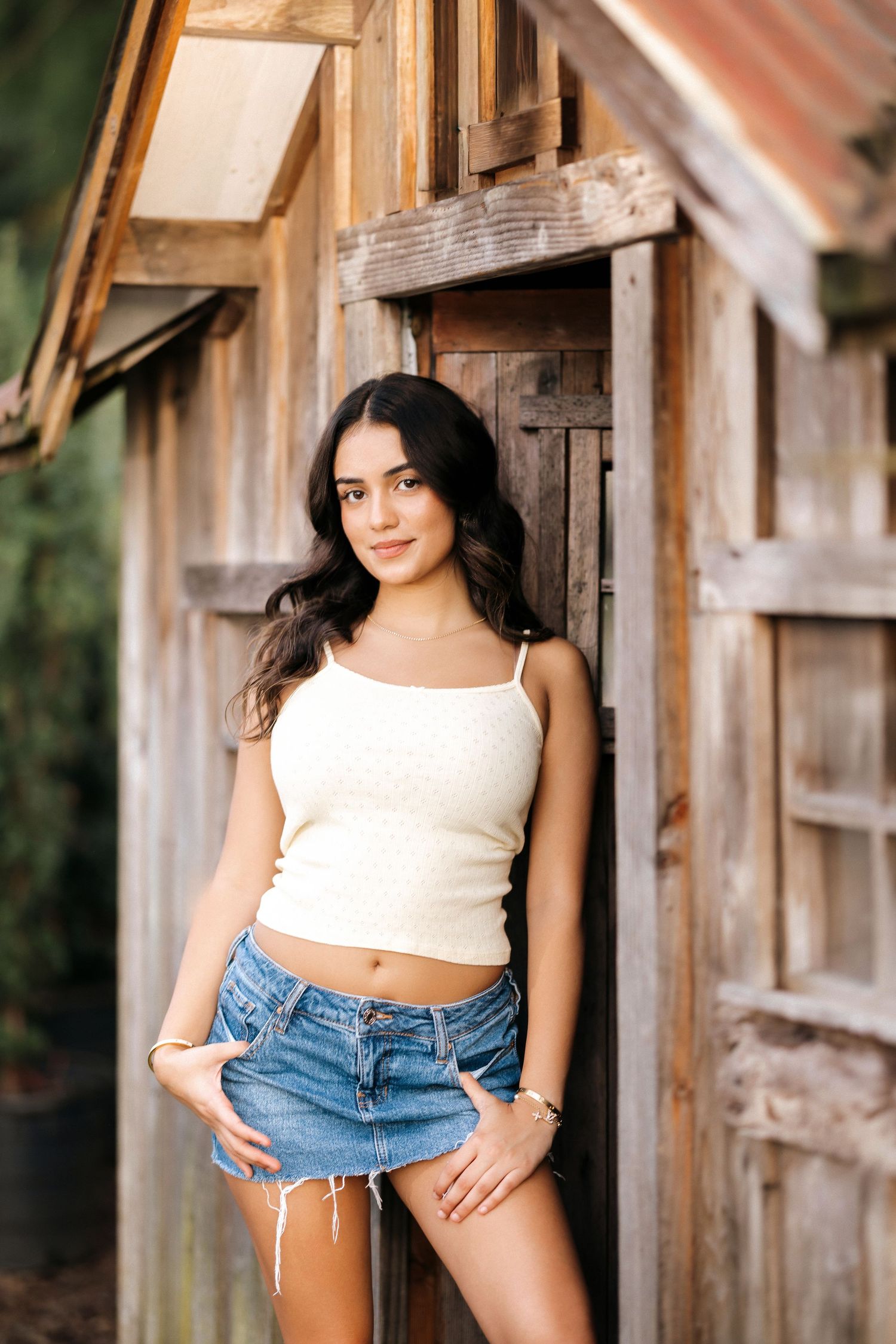 A rustic wooden barn wall provides a backdrop for a casual summer fashion photoshoot.