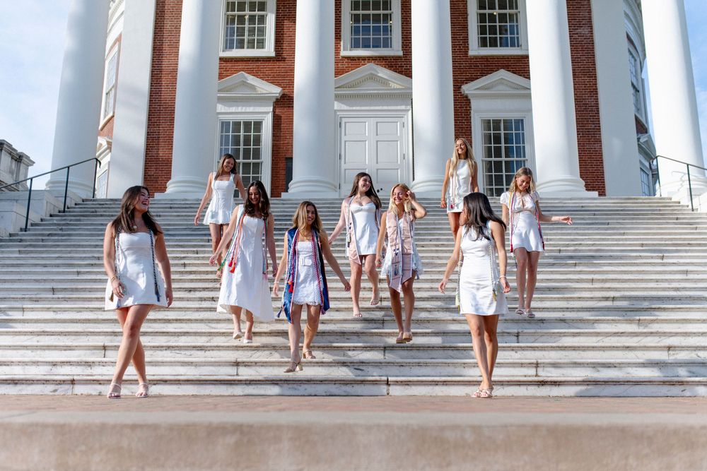 Group of young women in white dresses posing on grand steps of a classical building with white columns.