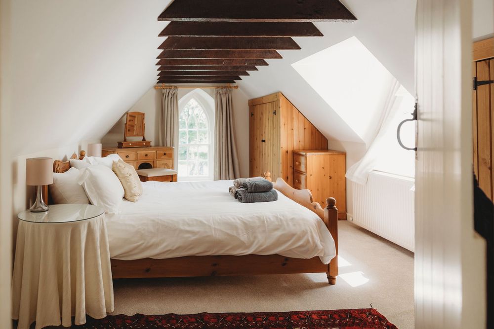 Cozy white bedroom interior with natural light streaming through windows and rustic wooden furniture.