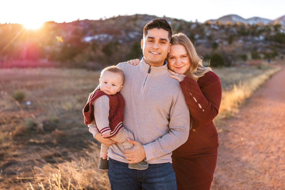Three people pose on a desert trail with warm sunset lighting behind them on a scenic mountain landscape.