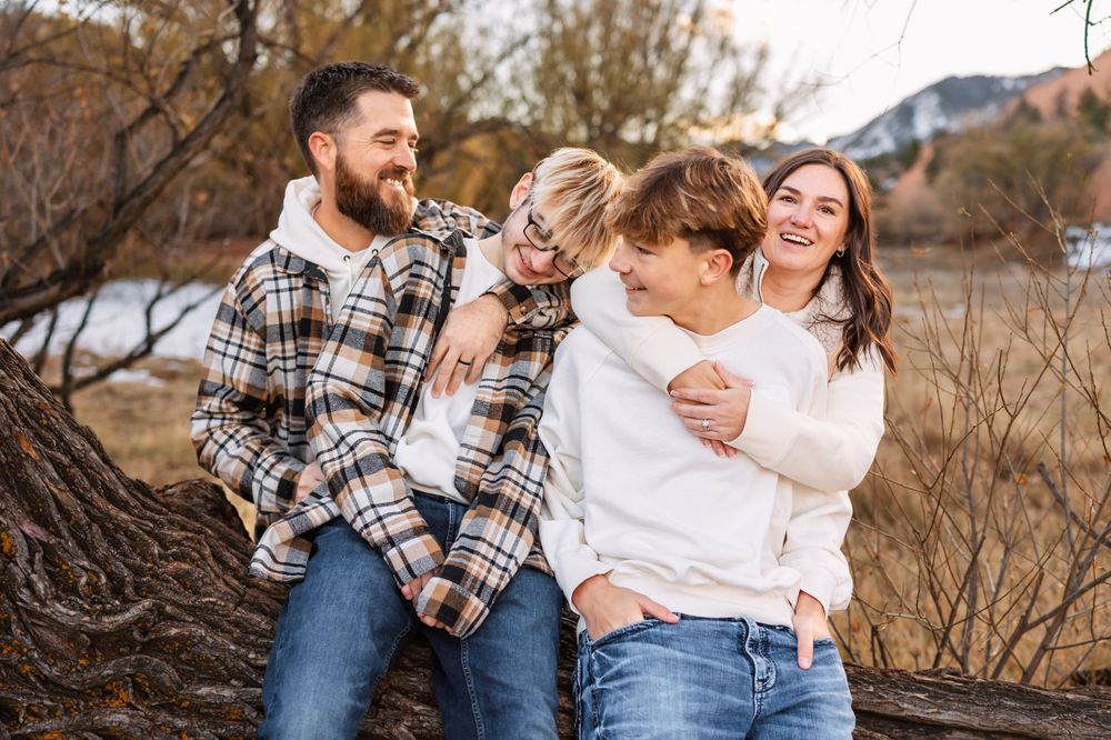A happy family laughs together while sitting outdoors in a natural setting during autumn.