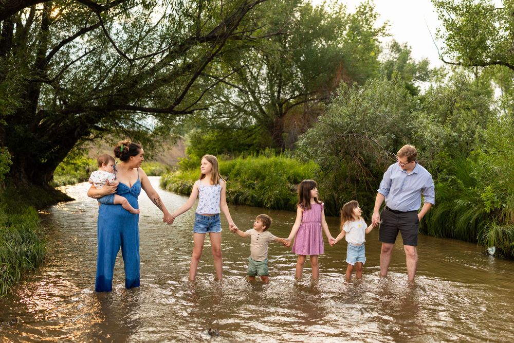 A group stands together in shallow water surrounded by lush greenery on a sunny summer day.