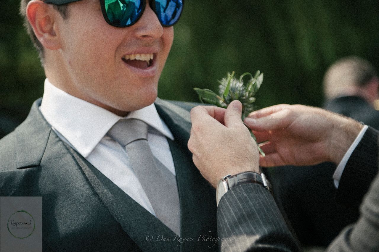 Reportage detail shot of groomsman having his buttonhole adjusted