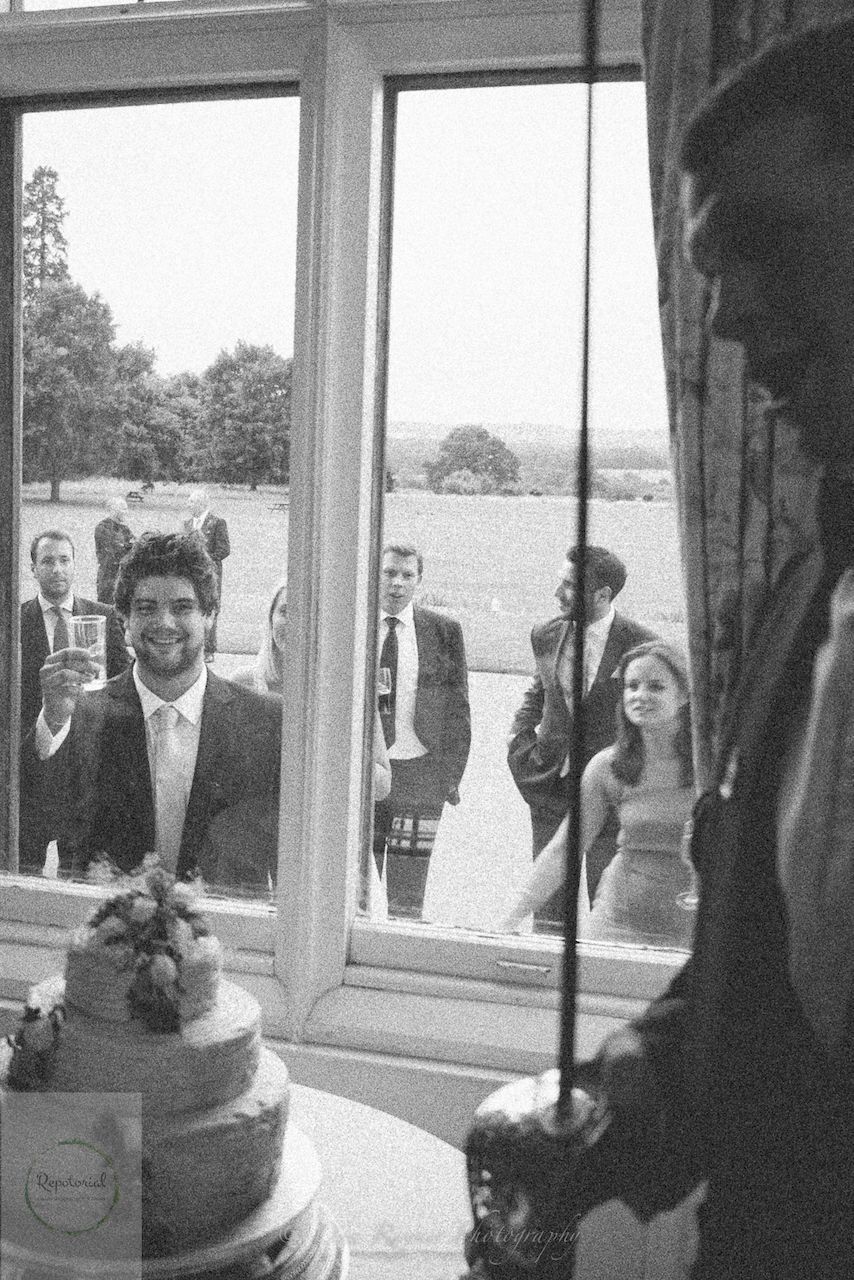 Wedding reportage photo of guests outside enjoying the reception taken from inside next to wedding cake