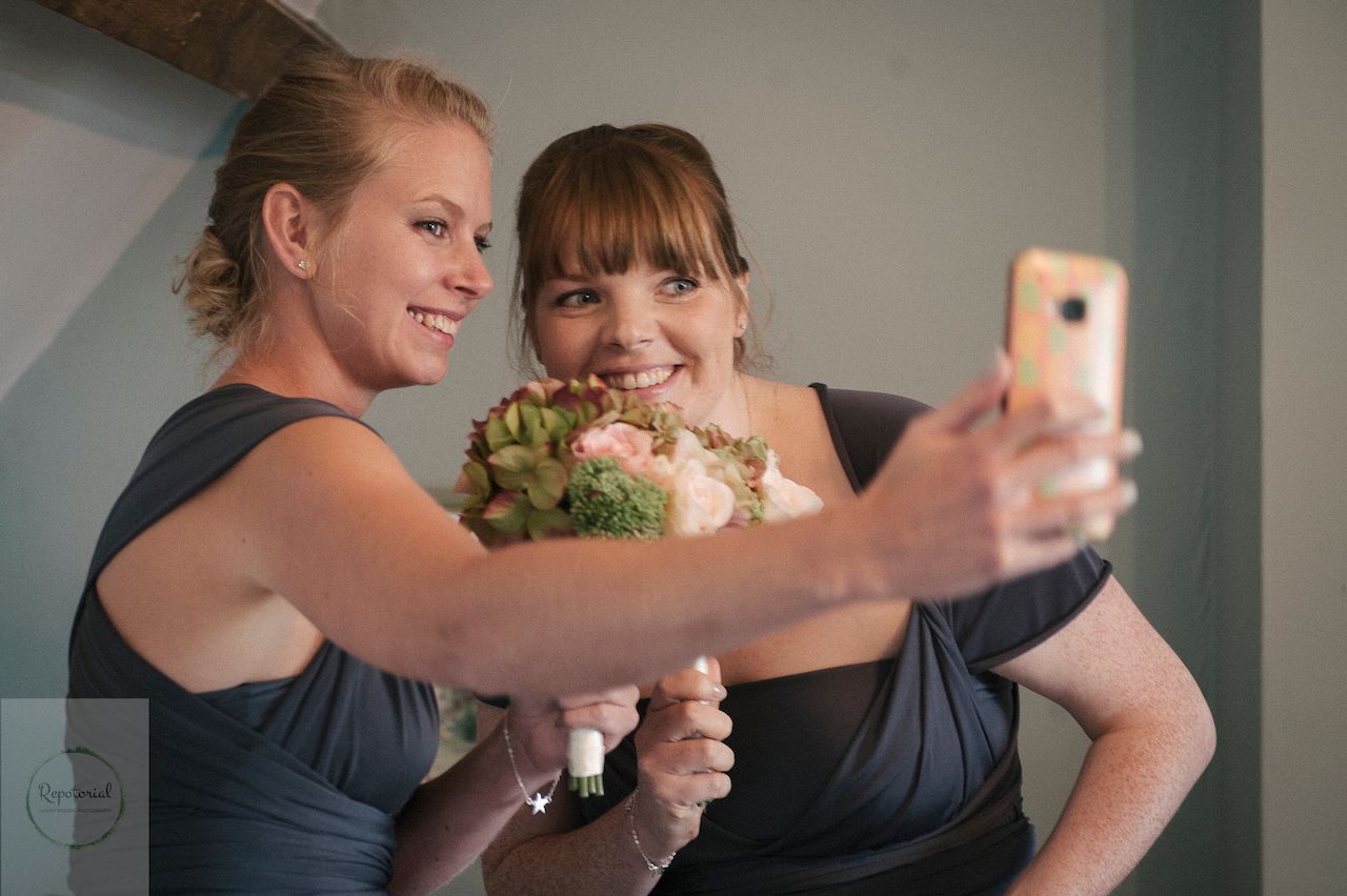 Wedding reportage photo of bridesmaids taking a selfie with flower bouquet