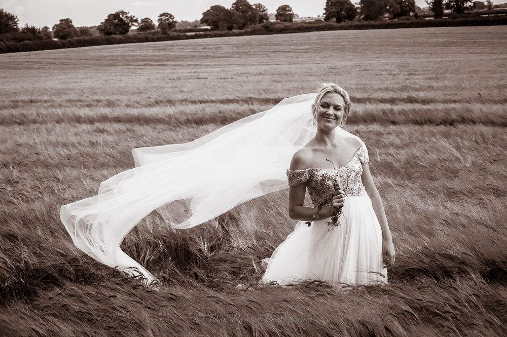 Wedding editorial portrait photo of bride posing in cotswold field with her veil flowing in the wind