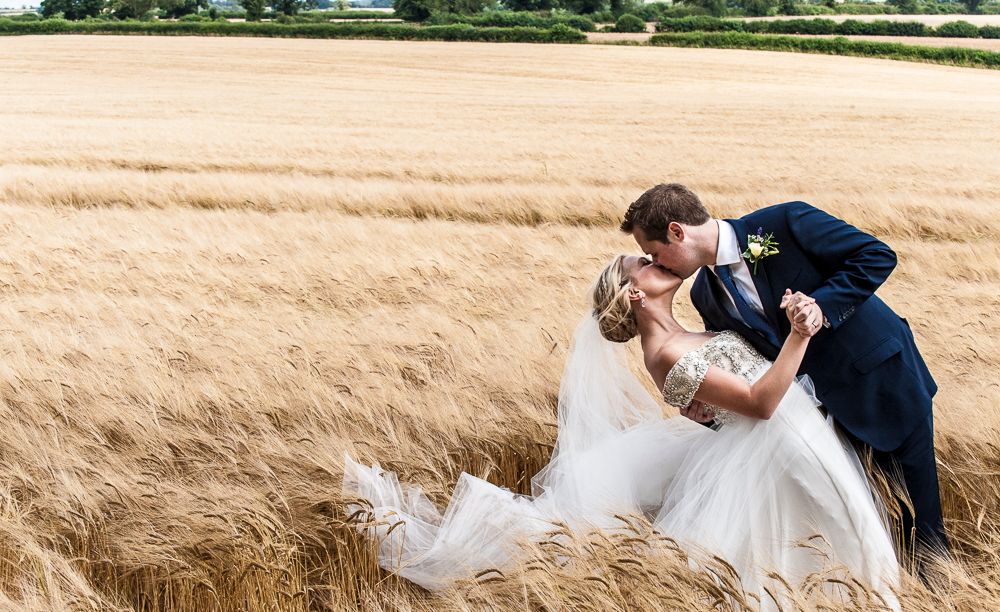 Editorial portrait of bride and groom kissing in cotswold field