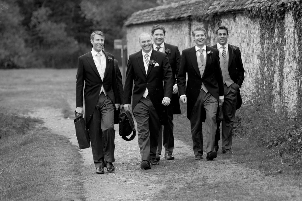 Wedding reportage photo of groomsmen walking to the ceremony in full morning suit and top hats