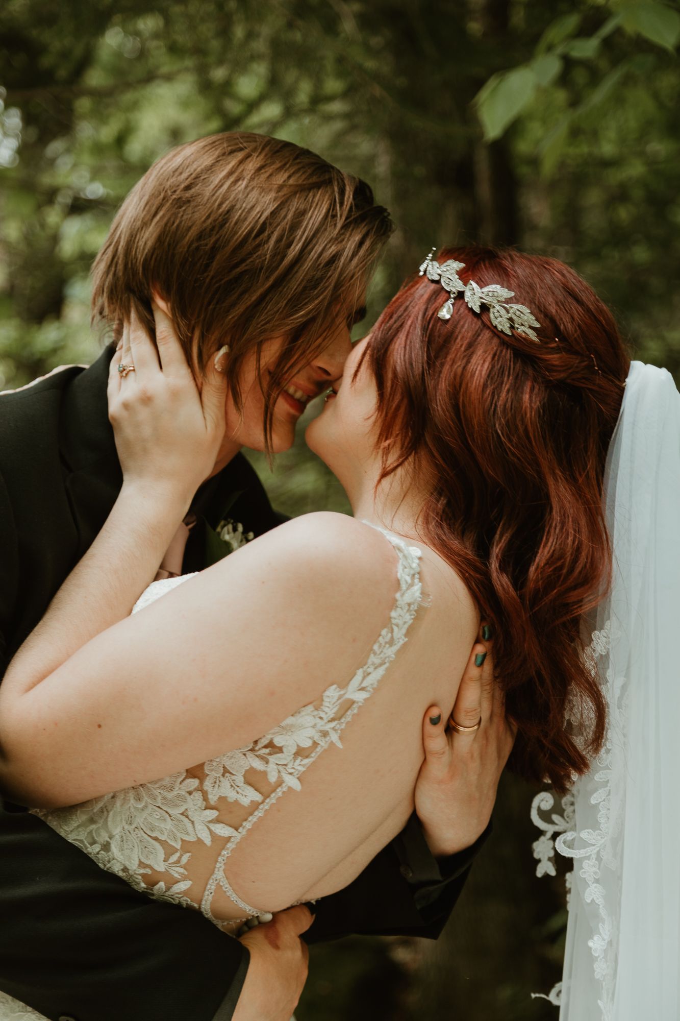 Close-up wedding photo showing delicate lace details on dress strap against a natural green backdrop.