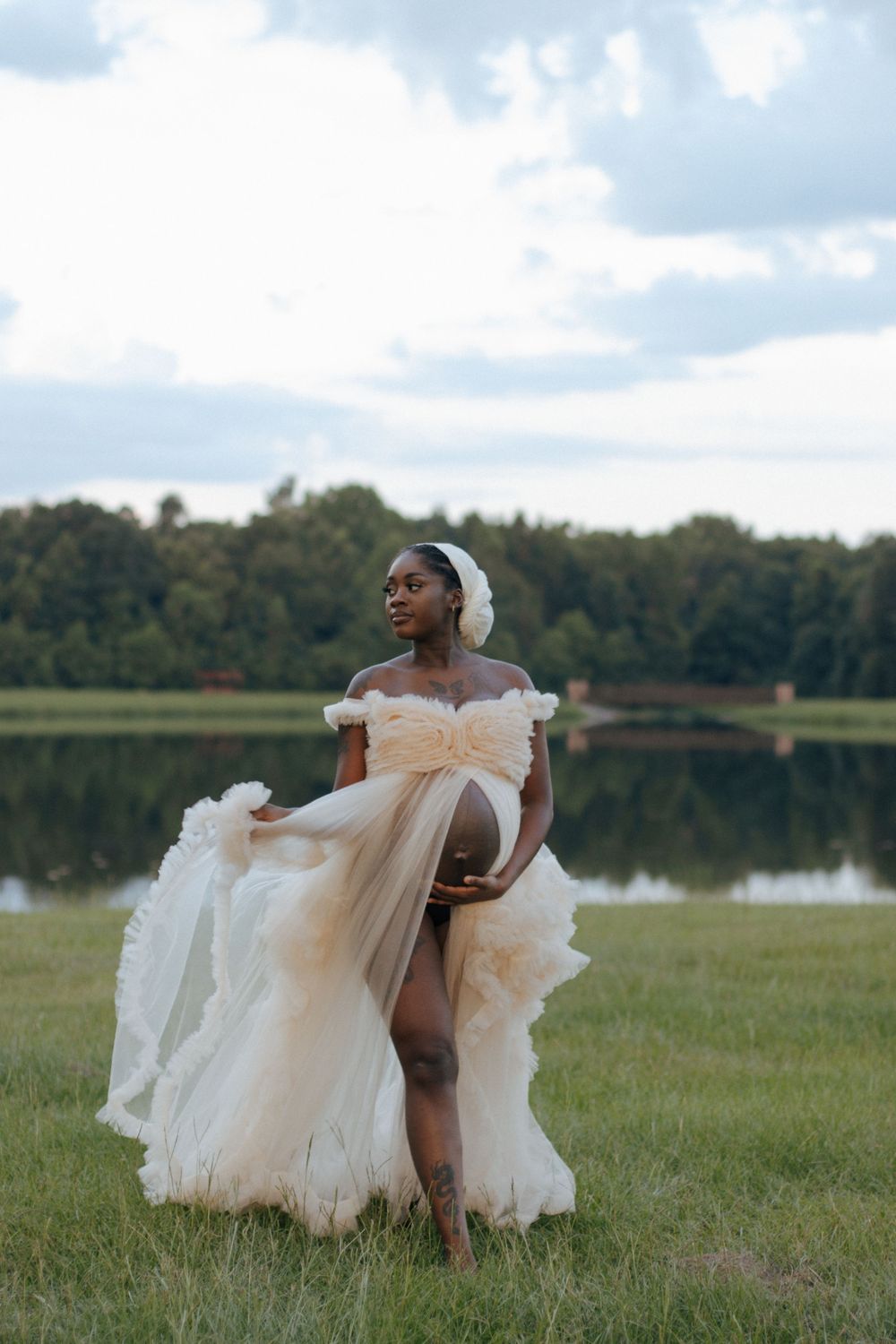 An elegant off-shoulder wedding dress flows gracefully in the breeze by a serene lake during a scenic outdoor photo shoot.