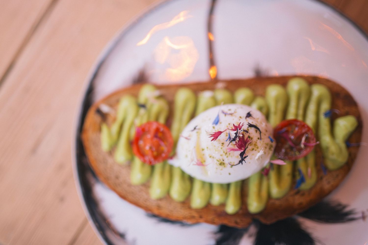 Avocado toast topped with a poached egg and red garnish on a decorative plate.