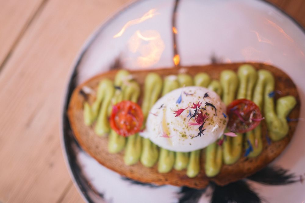 Avocado toast topped with a poached egg and red garnish on a decorative plate.