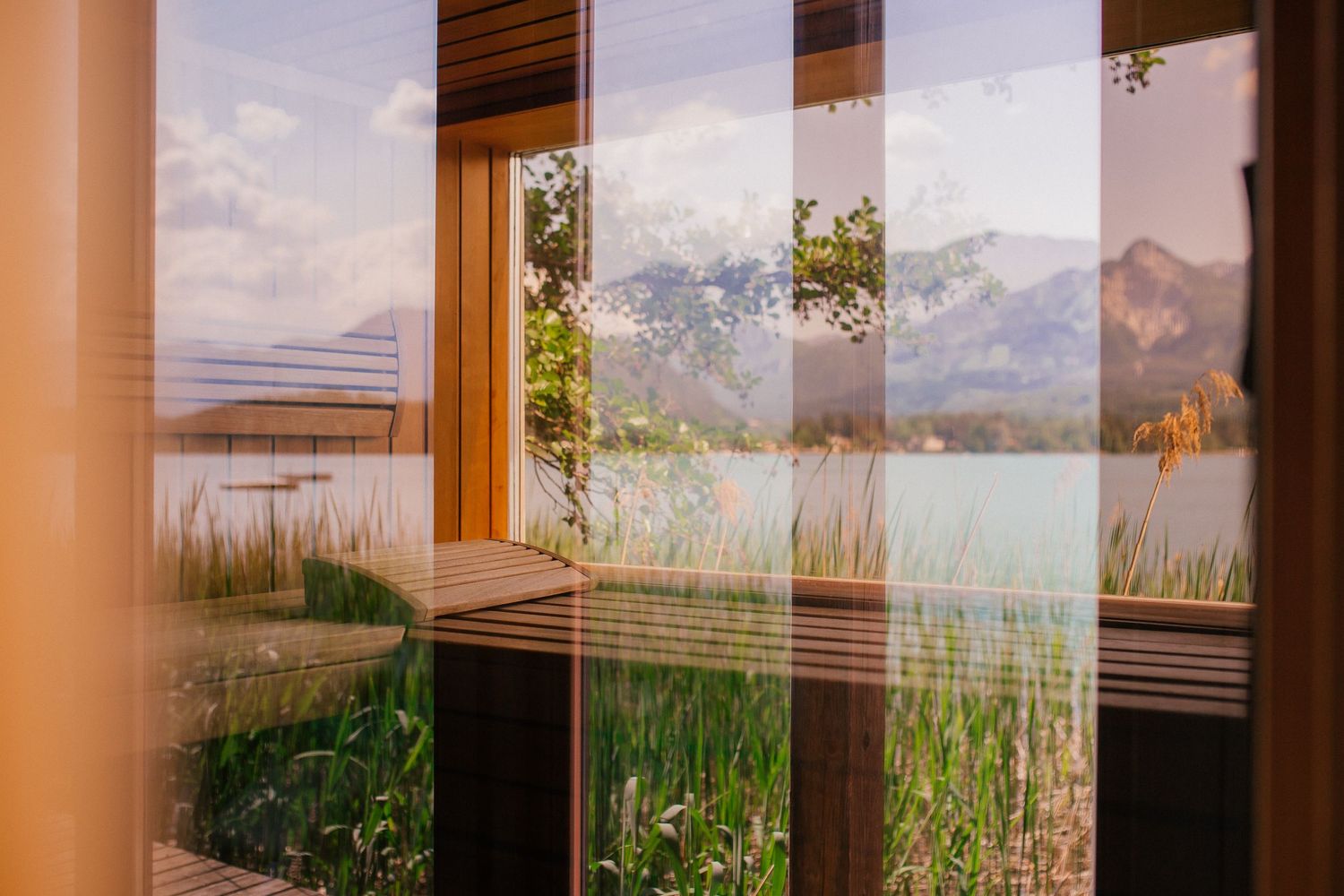 Scenic mountain lake view through window with tall grasses in foreground during sunset.