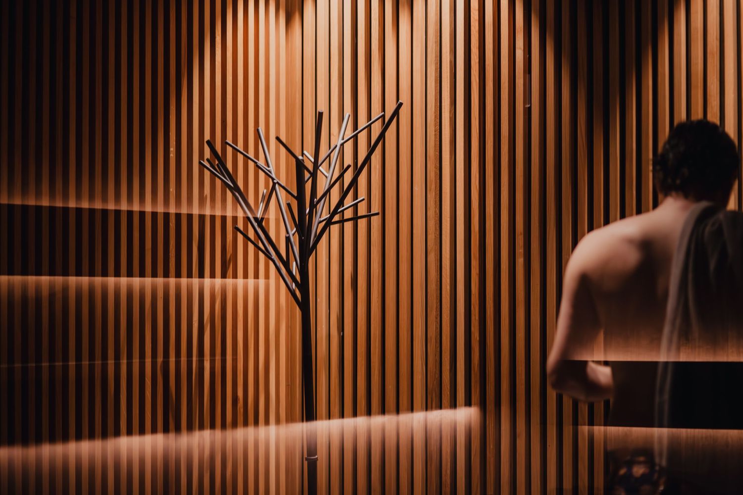 Modern spa interior with wooden slat walls and decorative bare tree silhouette in warm lighting.