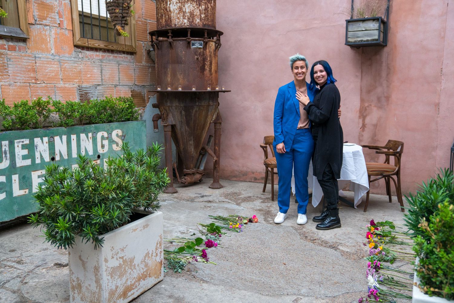 Couple poses in front of rustic brick wall with vintage signage.