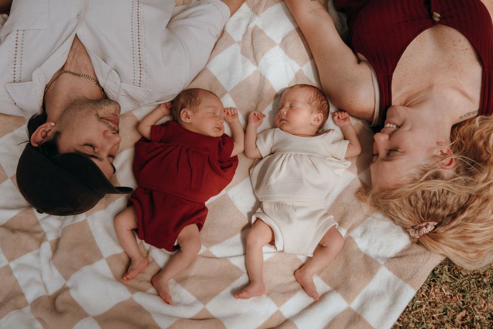 Aerial view of babies lying peacefully on white bedding while wearing red and white outfits.