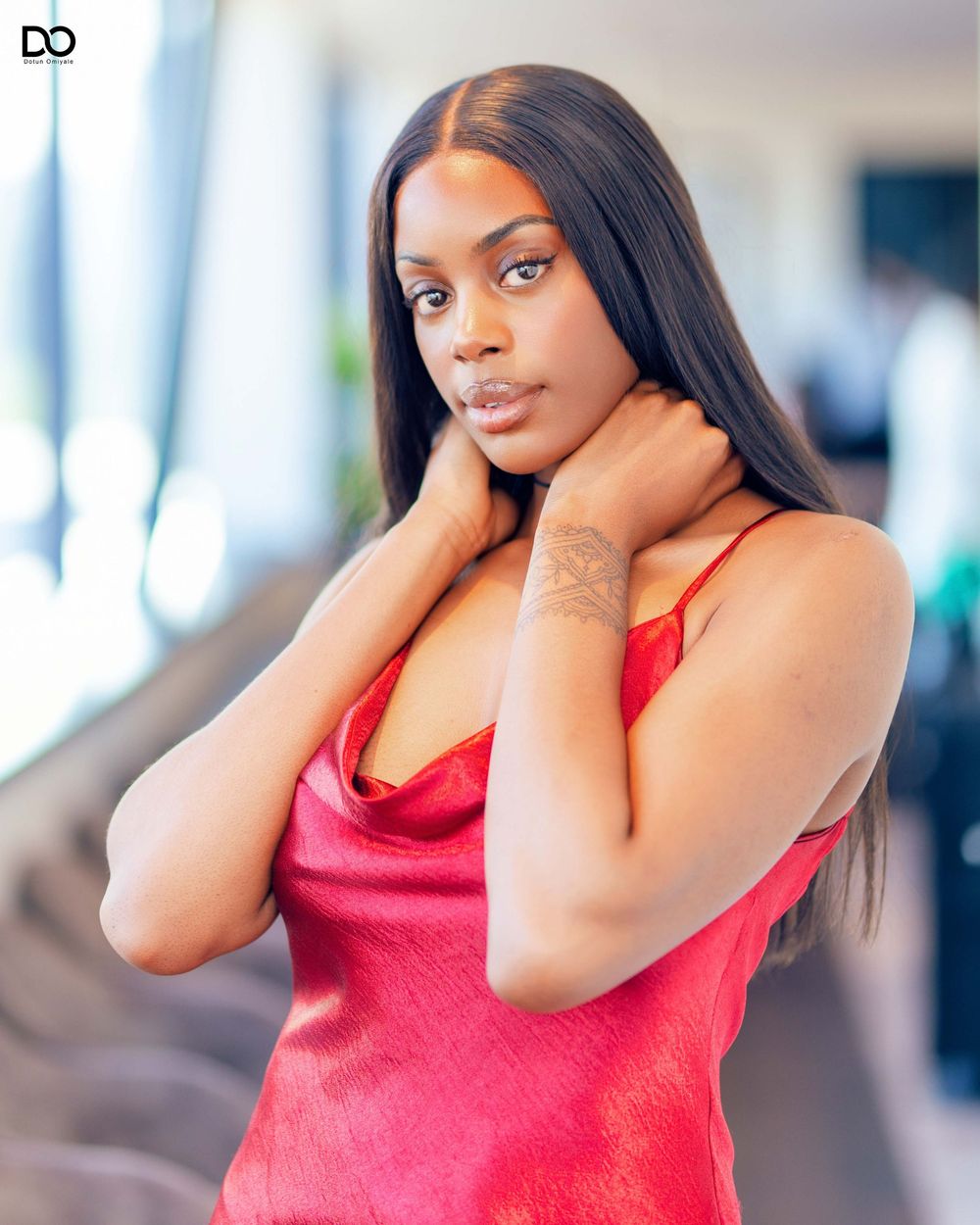 Woman in a coral tank top posing against a bright interior background.