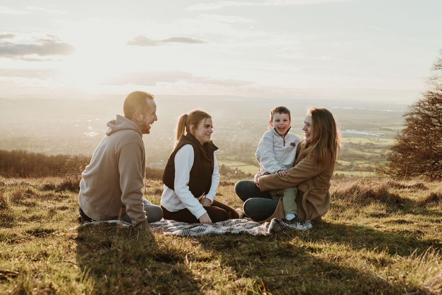 Friends enjoying a picnic on a hilltop during sunset with scenic countryside views.
