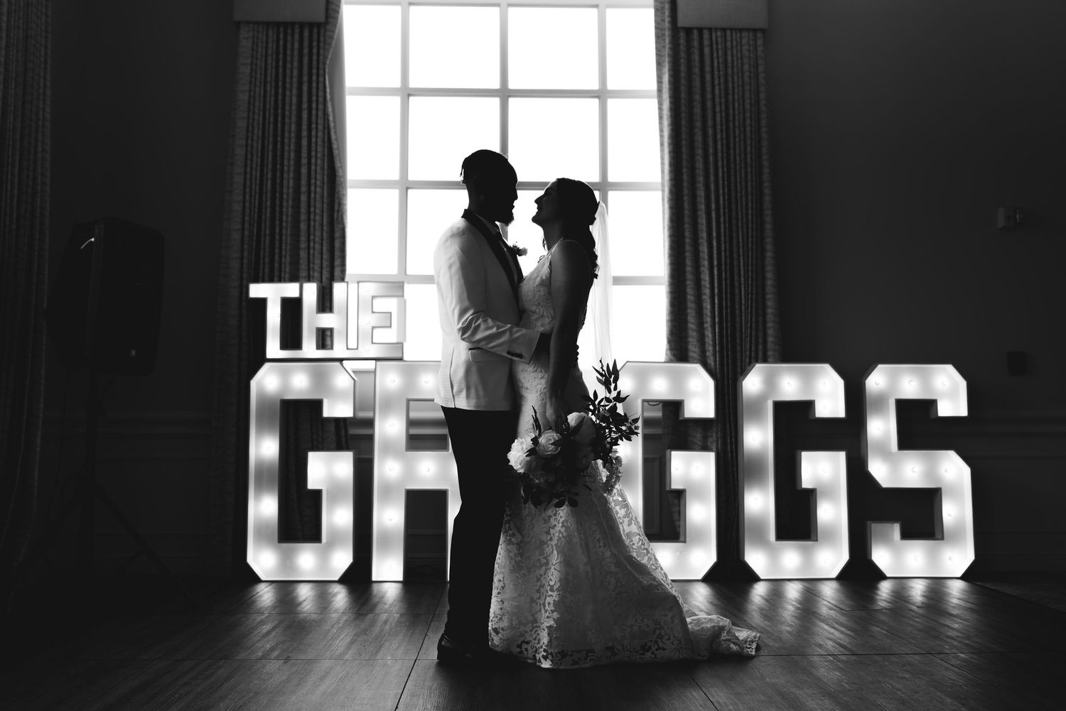 Romantic black and white silhouette of newlyweds dancing in front of illuminated GREGGS sign.