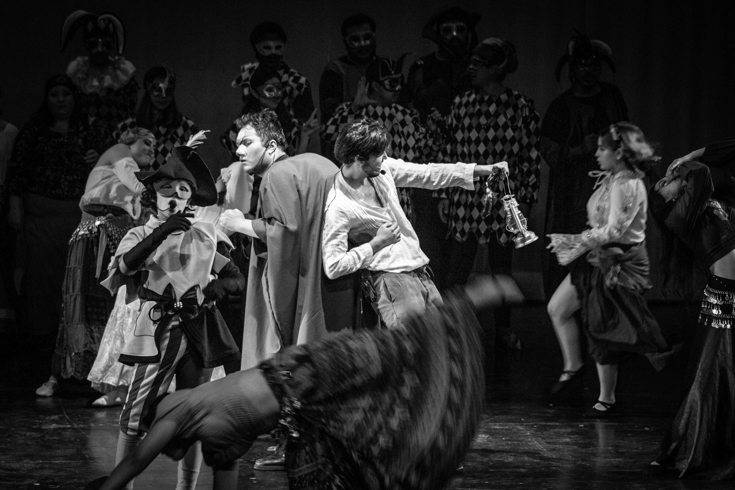 Black and white photo of performers in elaborate costumes dancing energetically on a theatrical stage.