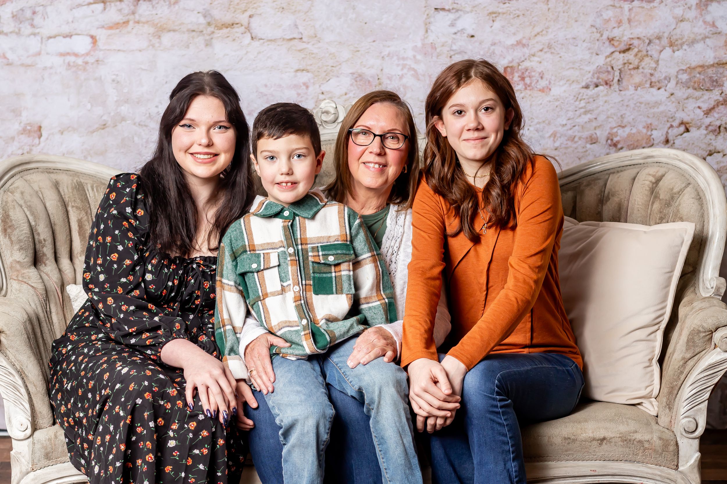 Family group seated on beige vintage couch against exposed brick wall.