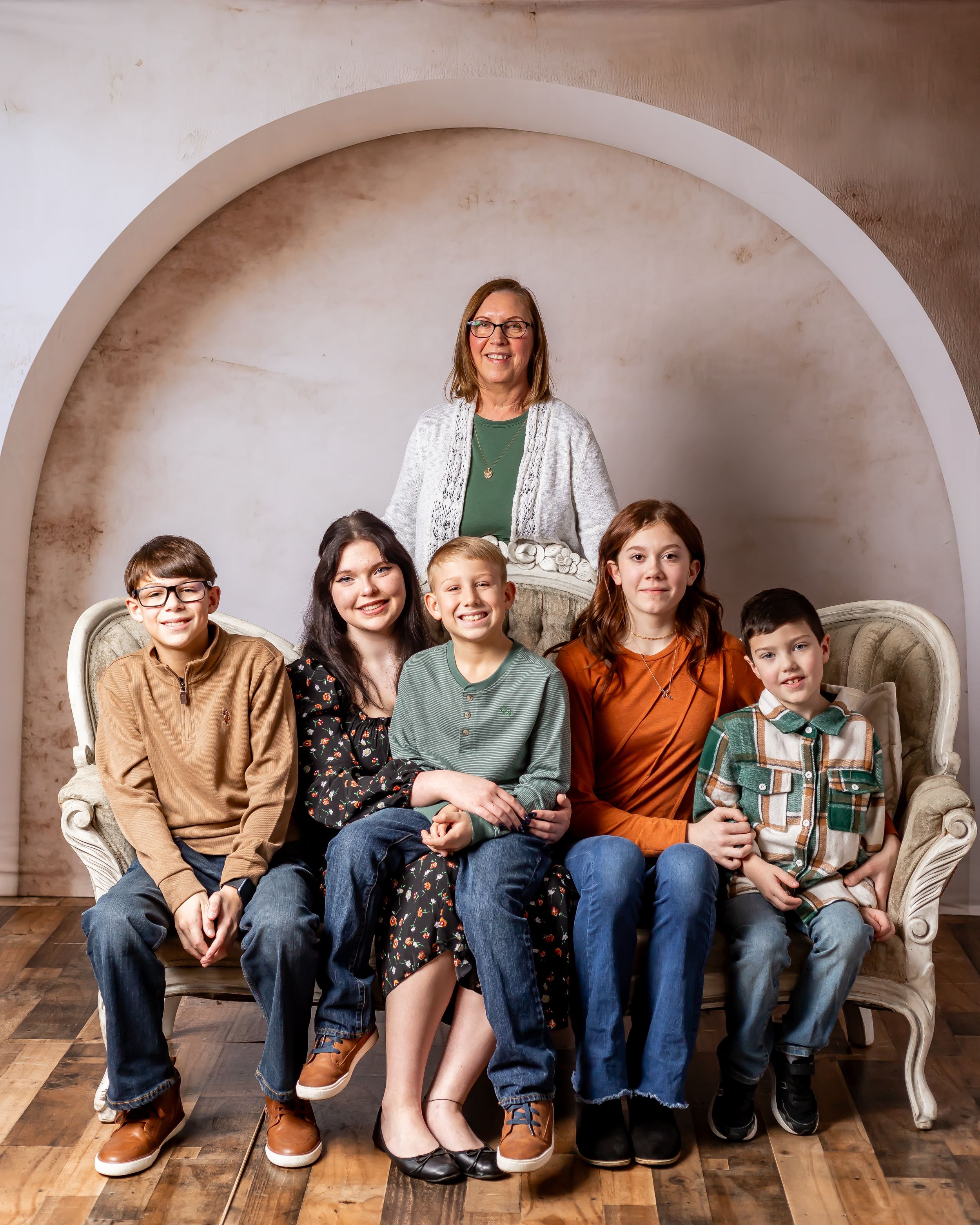 Family group portrait seated on vintage sofa under arched wall in studio setting.