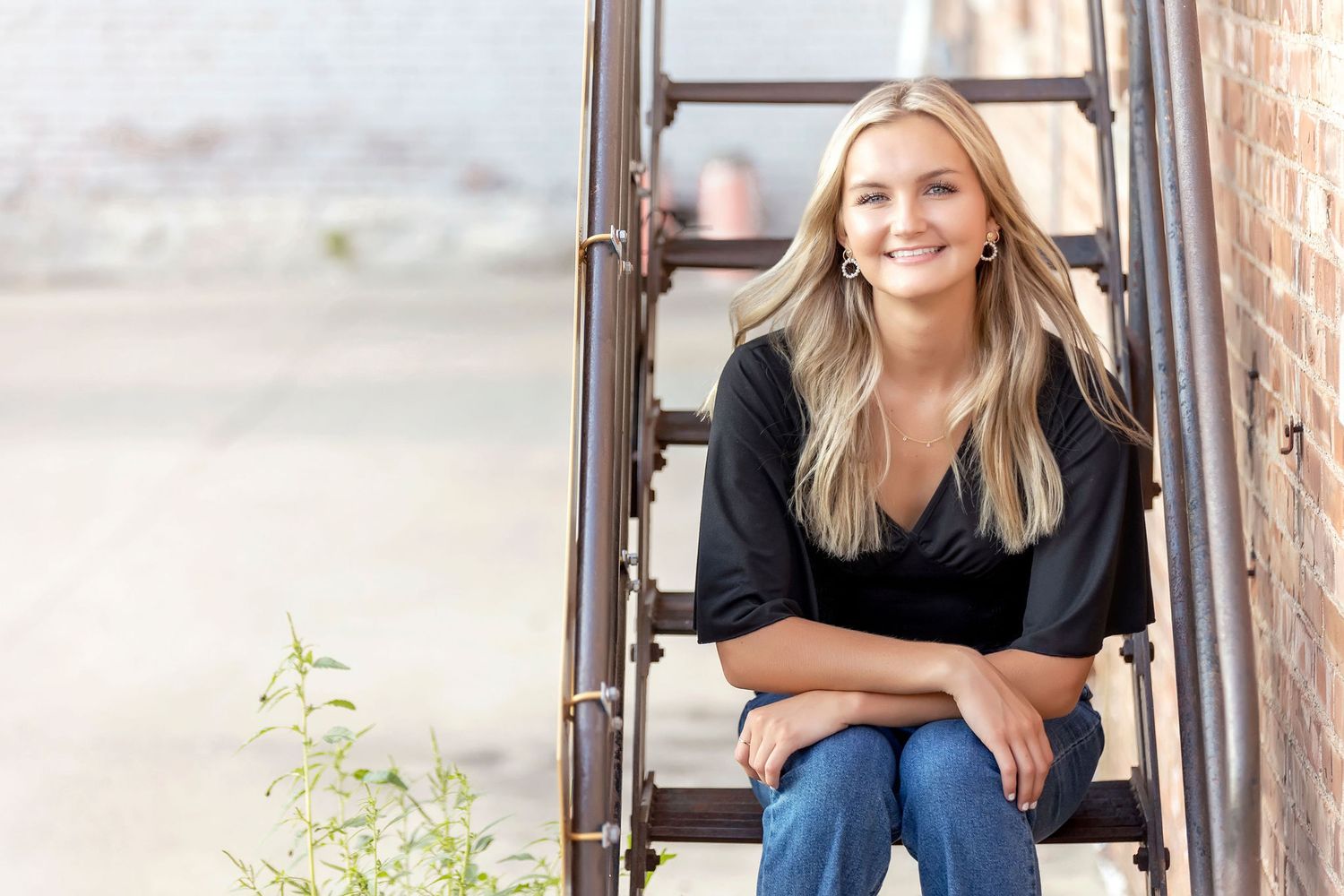 A casual portrait showing someone sitting on rustic metal stairs against an industrial brick wall background.