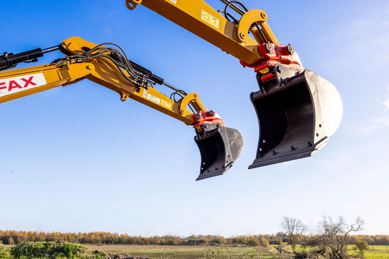 Two yellow excavator buckets positioned against bright blue sky in construction setting.