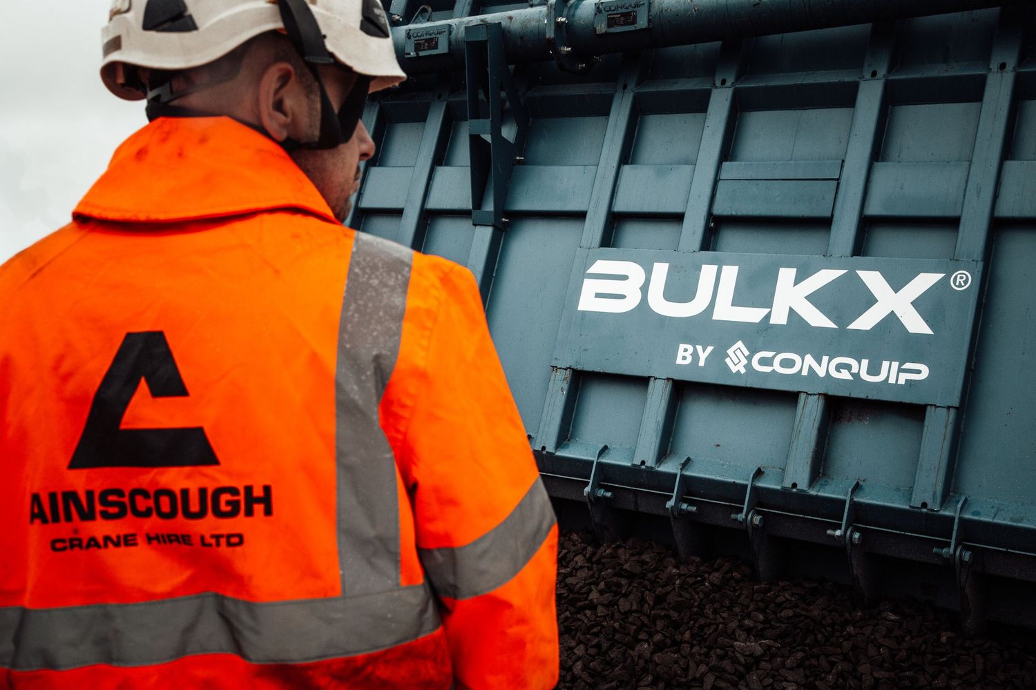 Workers in high visibility orange safety vests inspect a black shipping container with Bulk X branding.