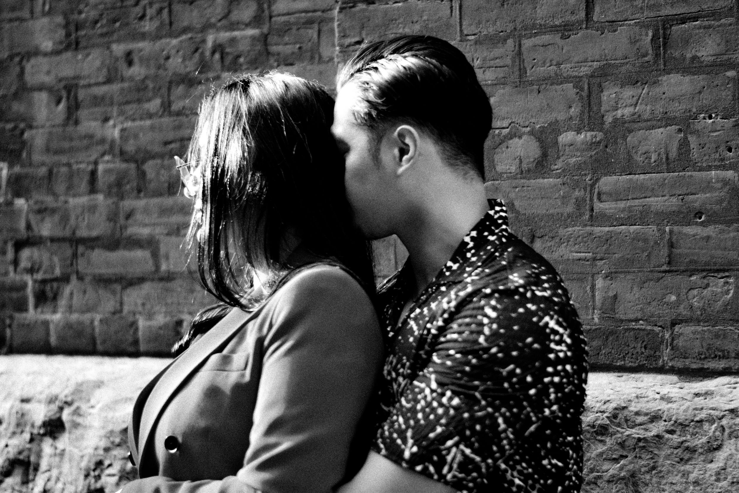Black and white photo of a couple sharing a romantic kiss against a rustic brick wall. Toronto GTA