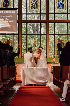 Bride and groom exchange vows at church altar with stained glass windows and red carpet aisle during wedding ceremony.