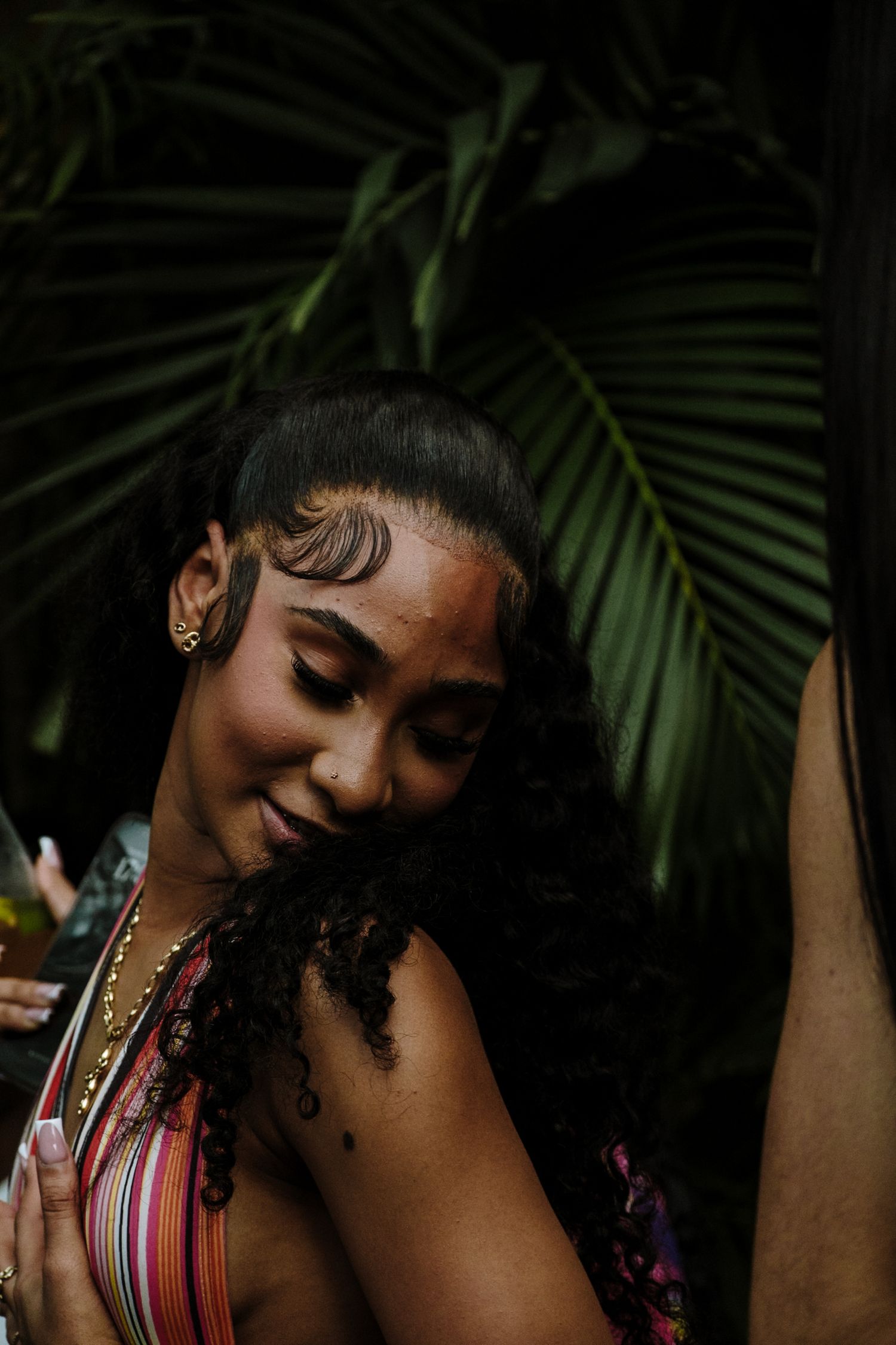 Beautiful festival attendee with curly hair and gold jewelry smiles against tropical palm leaves at night.
