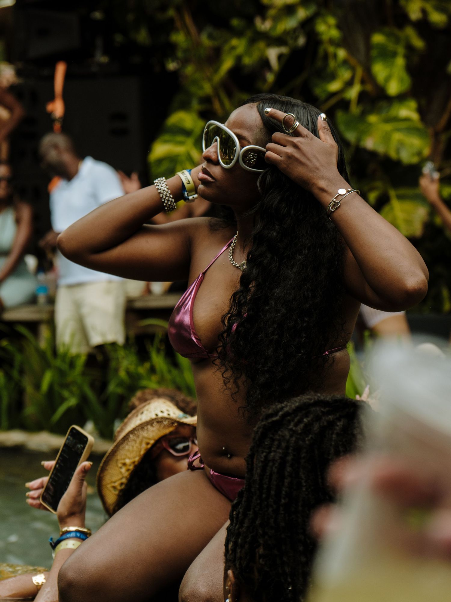 Woman in pink bikini with long dark curly hair enjoying a summer pool party while wearing sunglasses.