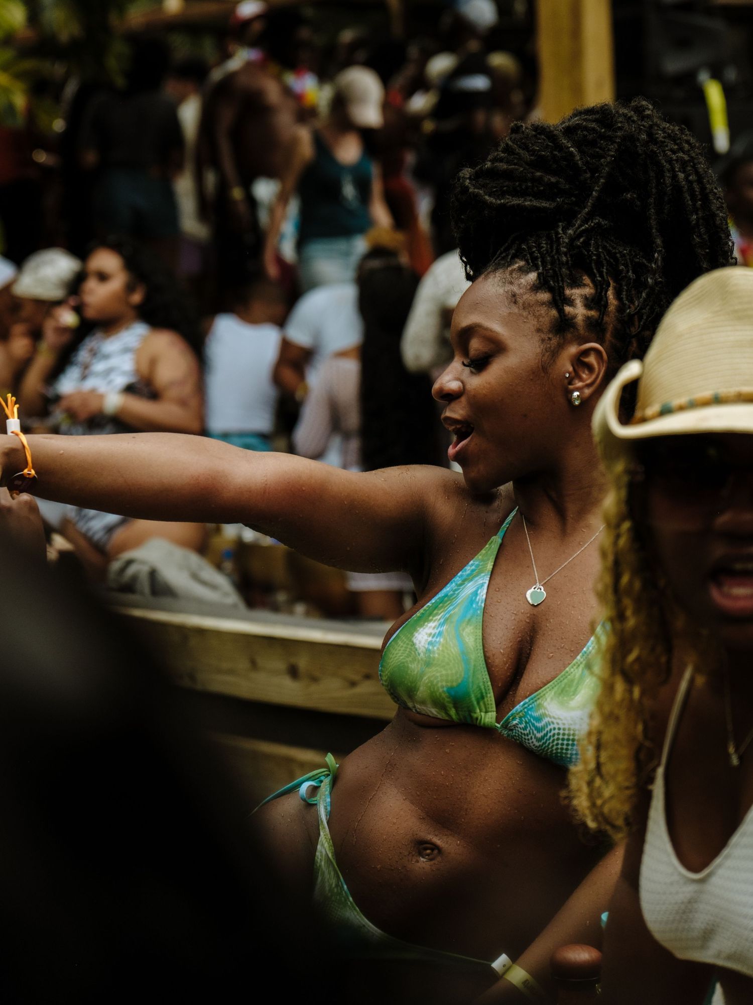 Dancing festival goer in turquoise bikini top celebrates with raised arm during outdoor summer event.