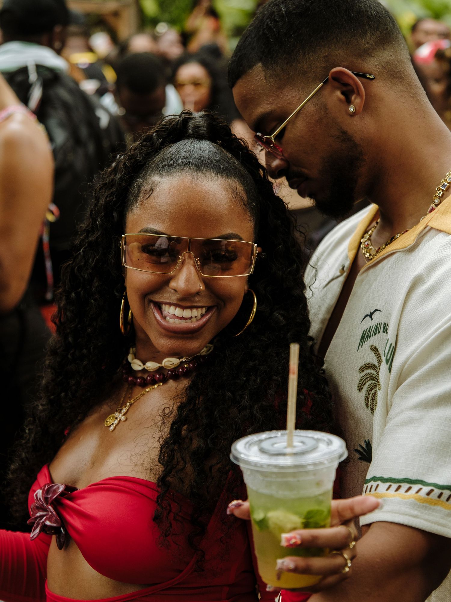 A couple shares a happy moment at an outdoor event, with one holding a green beverage in a clear plastic cup.