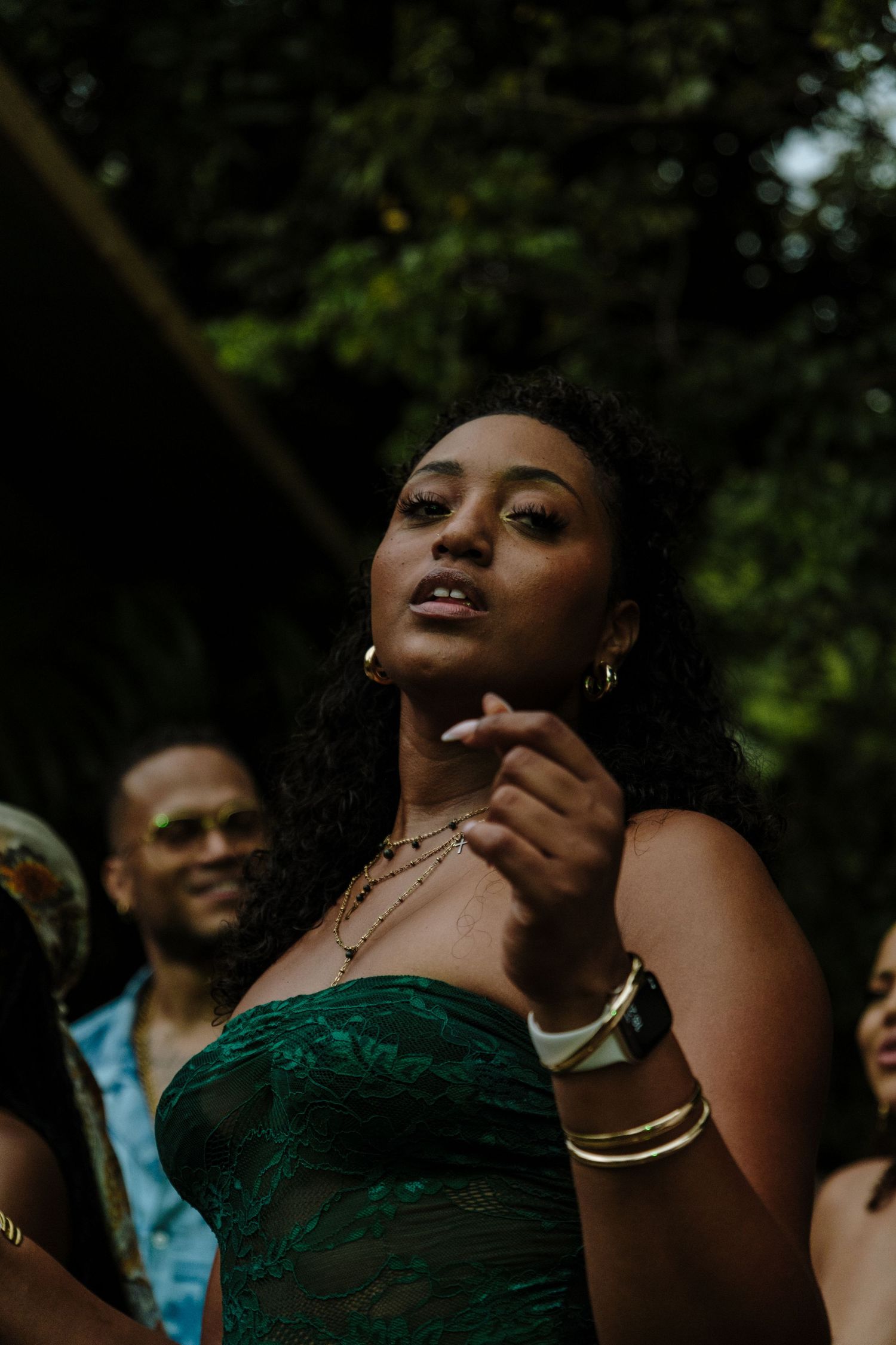 Person in a green strapless dress dancing outdoors while wearing jewelry and bangles.