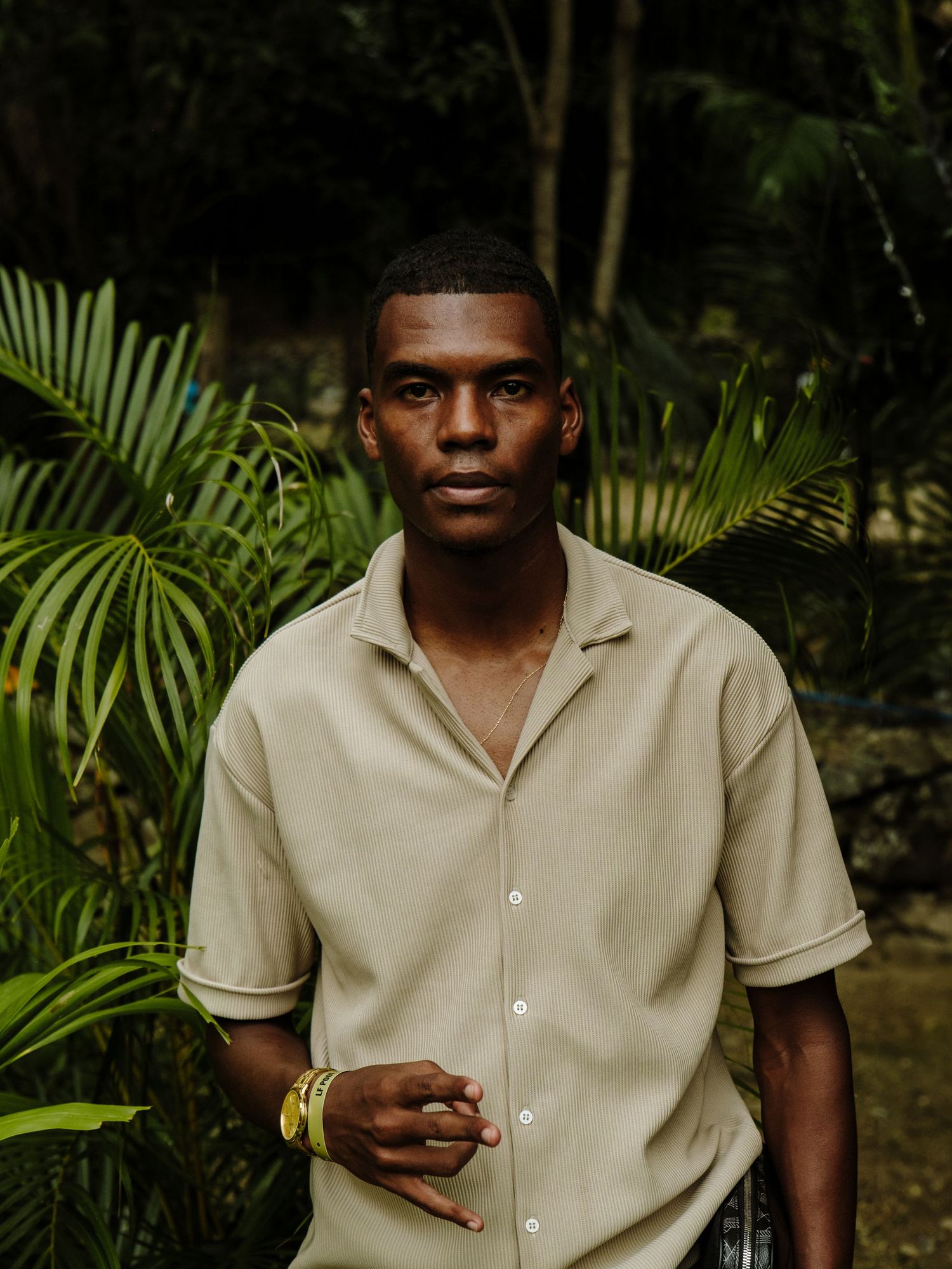 Portrait in nature with beige short sleeve button down shirt against lush tropical palm leaf background.